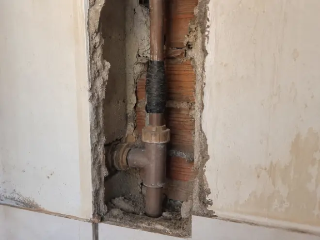 Parede aberta mostrando tubulação PVC marrom com emenda improvisada e fita preta em imóvel residencial - Serviços Hidráulicos em Capão da Canoa RS.